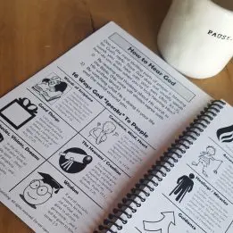 Open book with illustrated instructions and a white cup on a wooden surface.