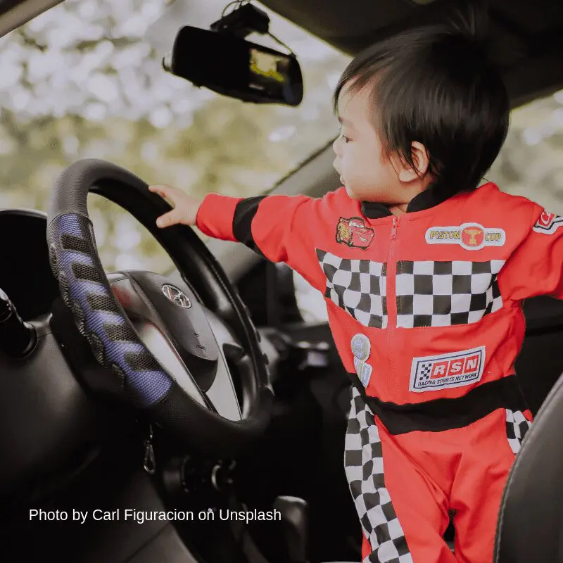 Child in race car outfit by steering wheel.