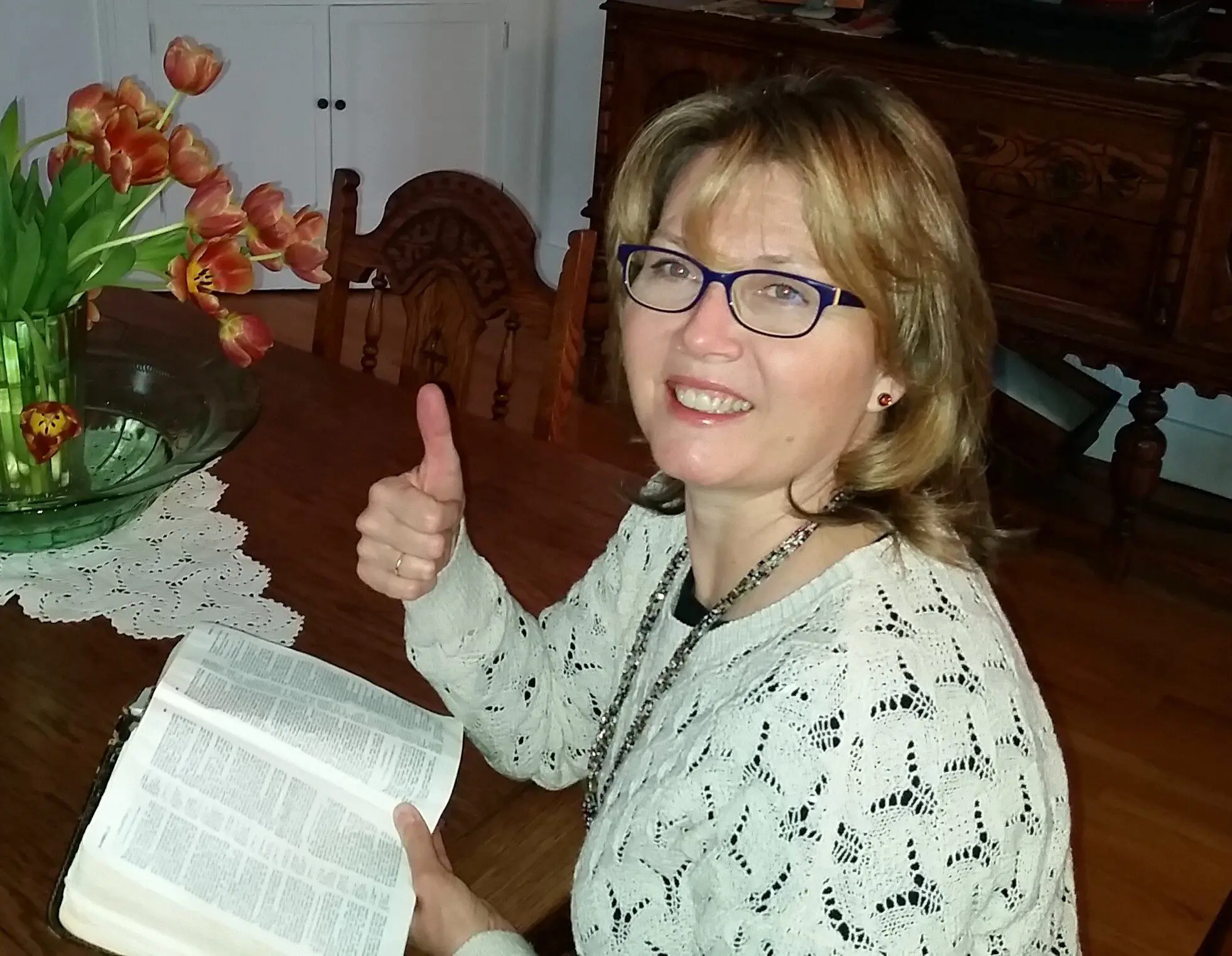 Smiling woman giving thumbs up while reading a book.