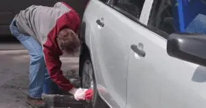 Person cleaning a white car's wheel and body with a cloth.