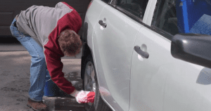 Person cleaning a white car's wheel and body with a cloth.