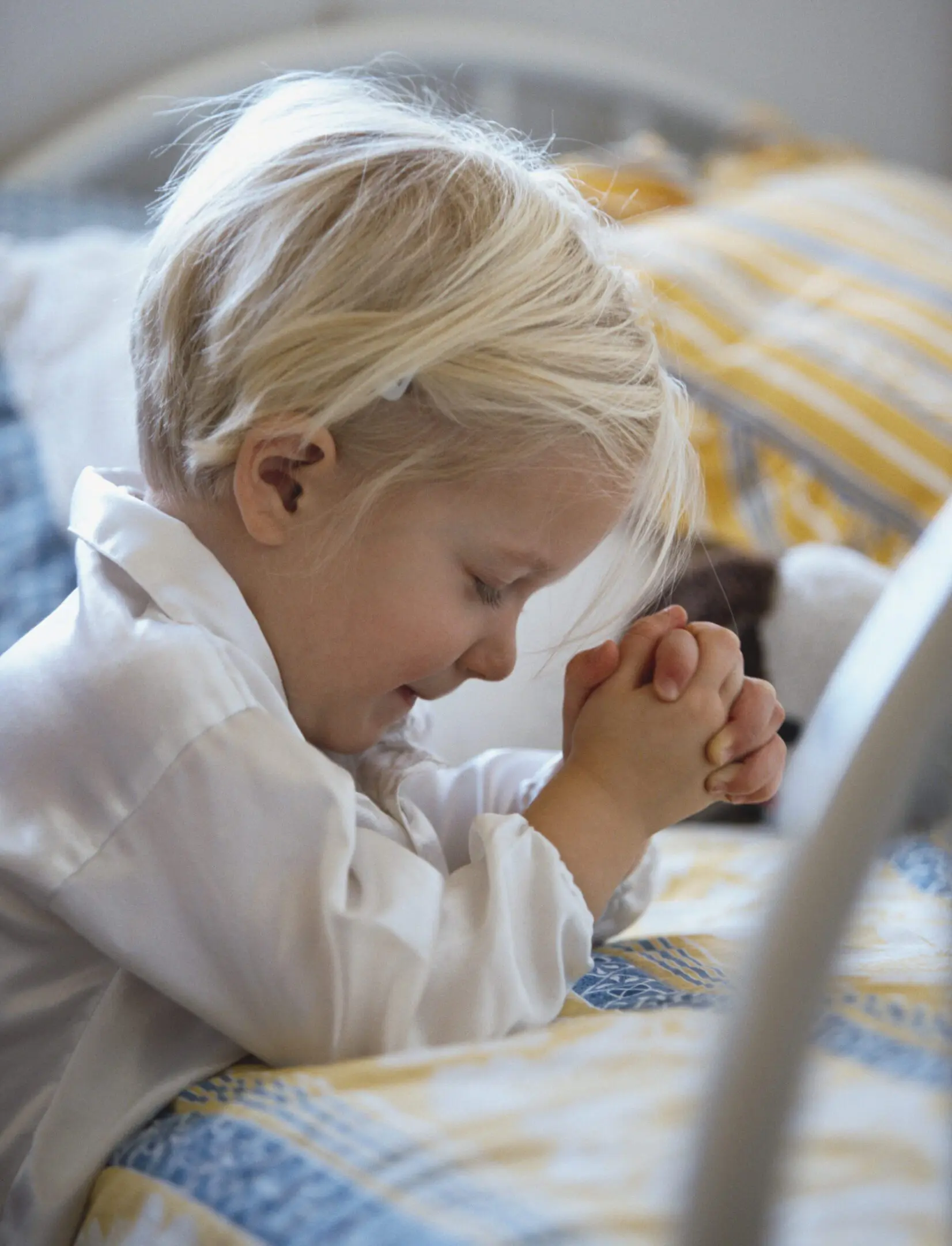 A young child with blonde hair praying with eyes closed.