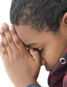 A child with eyes closed holding hands near face, appearing thoughtful or praying.